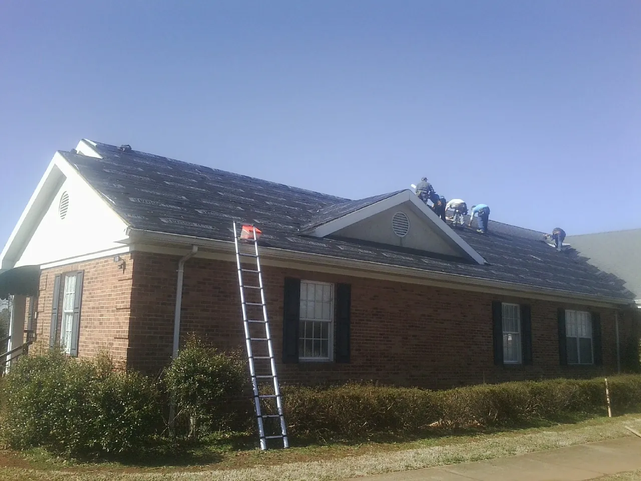 Crew tearing shingles off a brick ranch roof with a ladder set — Emergency Roof Repair work by our crew in Bellows Falls