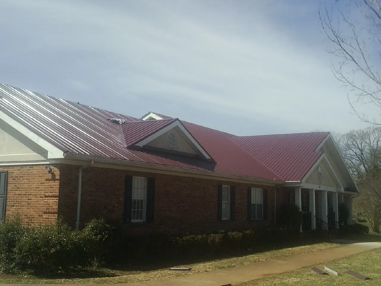 Red metal roof with gabled entries on a long brick building, from a Hail Damage Roof Repair job in Bellows Falls