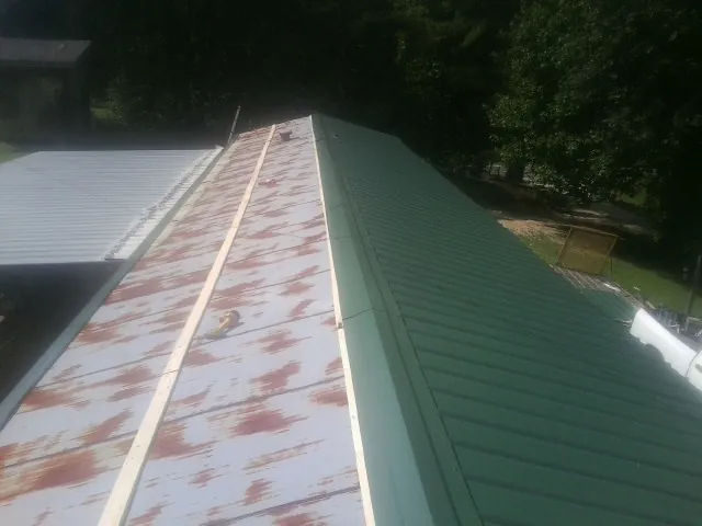 Old rusted panels beside newly installed green metal roofing — Wind Damage Roof Repair by Roofing Brothers in Bellows Falls