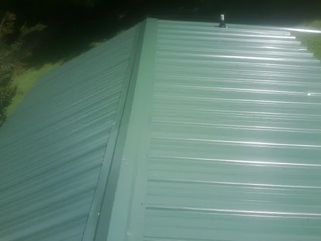 New green metal panels meeting at the ridge of a roof — Flat Roof Repair work by our crew in Bellows Falls