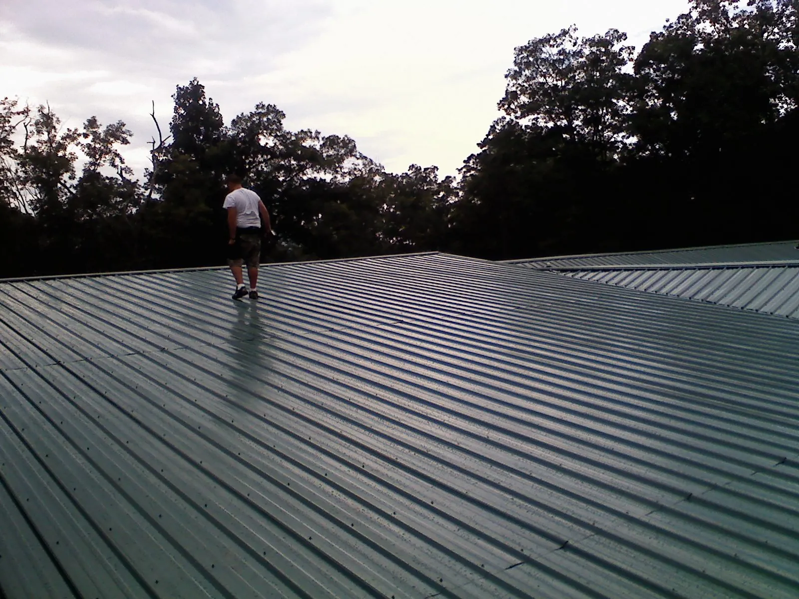 Roofer walking a wide expanse of new green metal roofing in Bellows Falls
