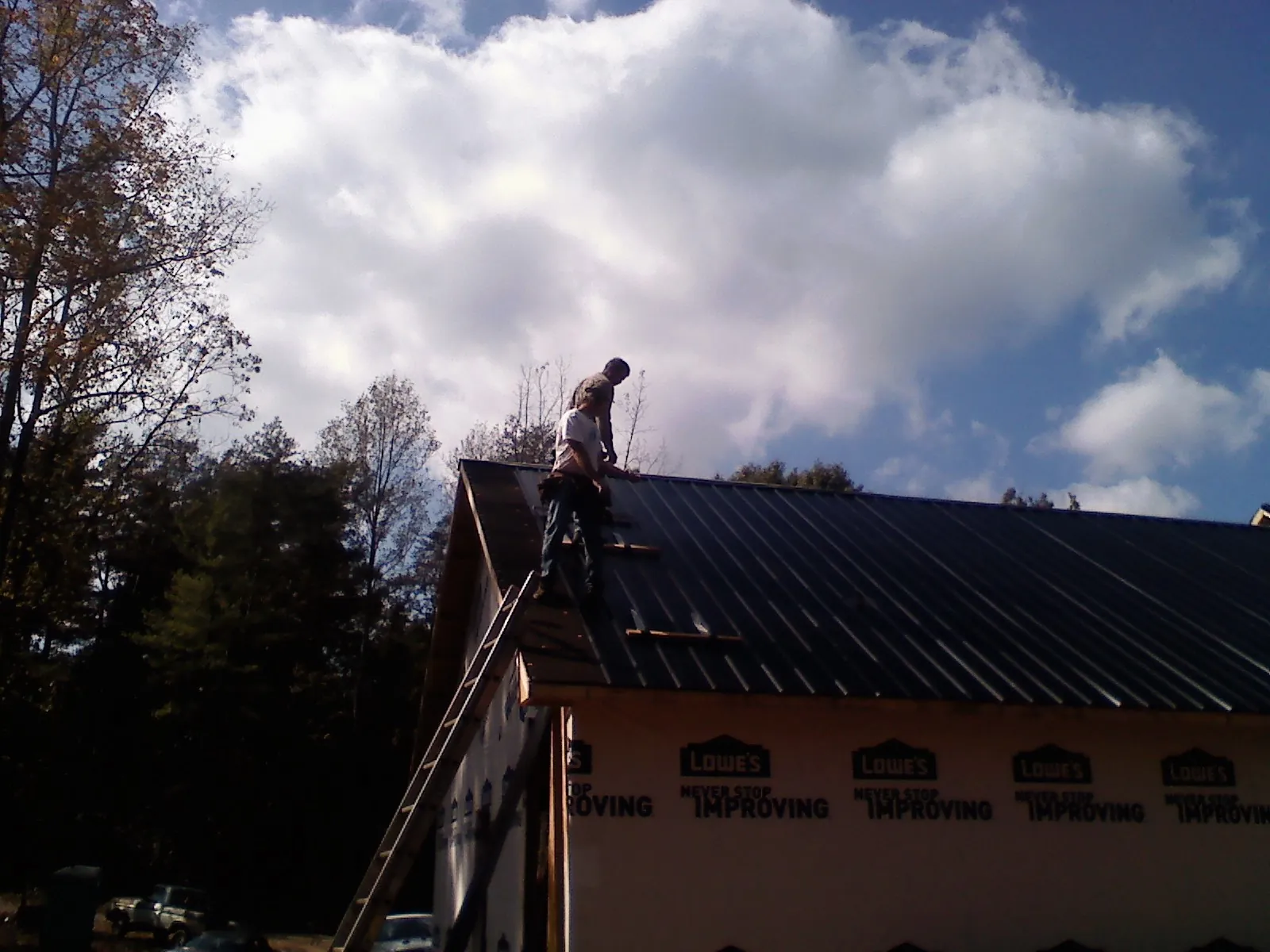 Roofer fastening dark metal panels high against a cloudy sky, from a Roof Inspection job in Bellows Falls