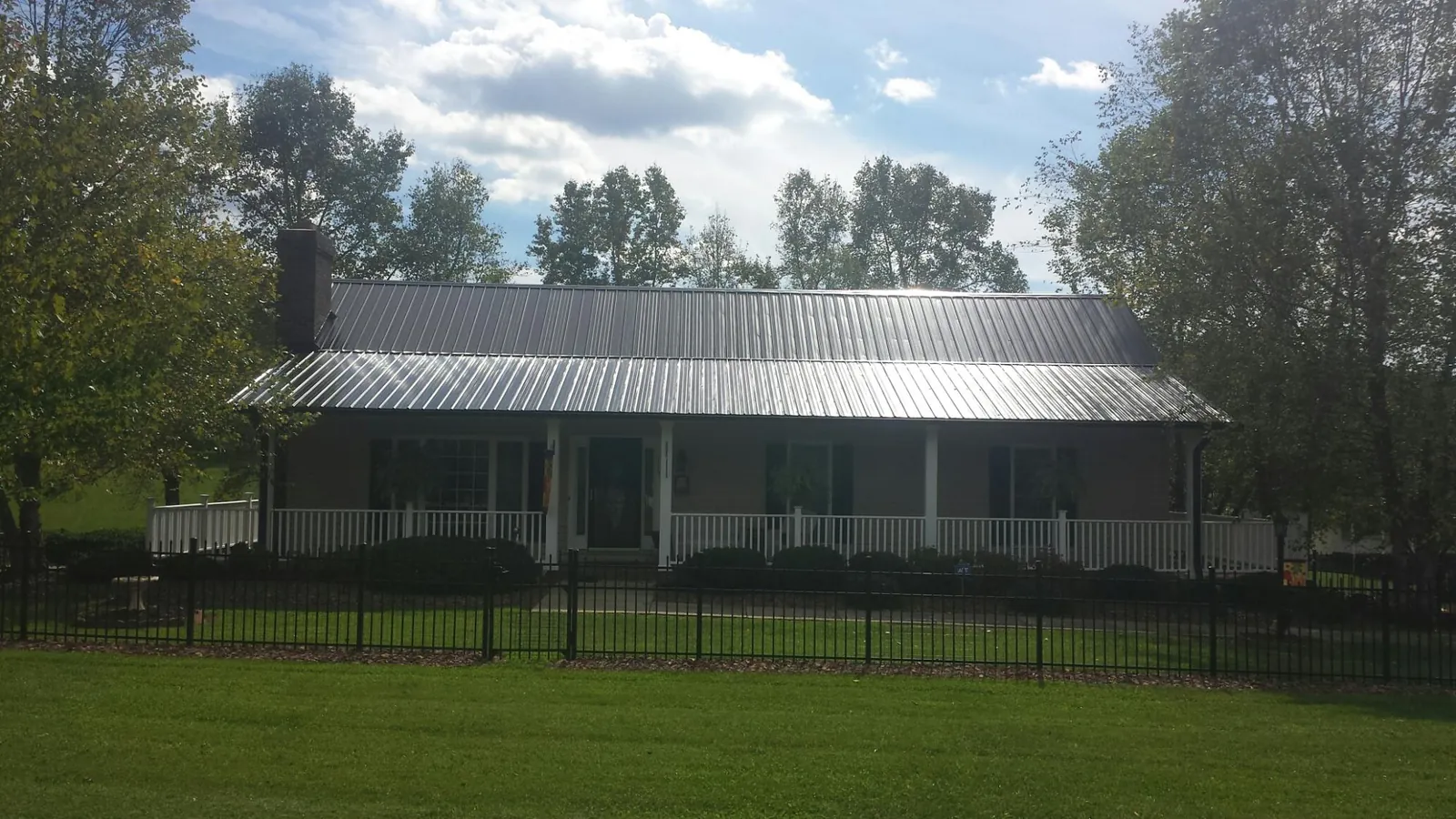 Gray metal roof on a brick ranch with a full width front porch — Gutter Guard Installation work by our crew in Bellows Falls